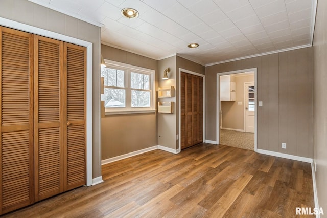 unfurnished bedroom featuring multiple closets, crown molding, baseboards, and wood finished floors