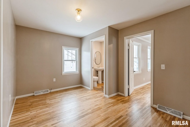 unfurnished bedroom featuring light wood-style floors, baseboards, visible vents, and a sink