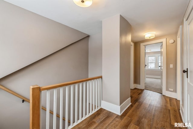 hall with dark wood-type flooring, an upstairs landing, and baseboards