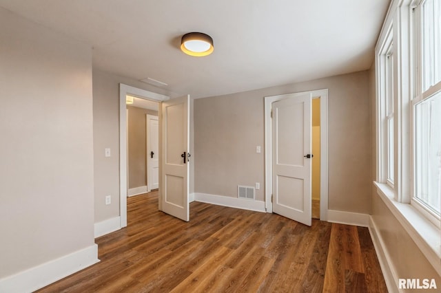 unfurnished bedroom with dark wood-type flooring, visible vents, and baseboards