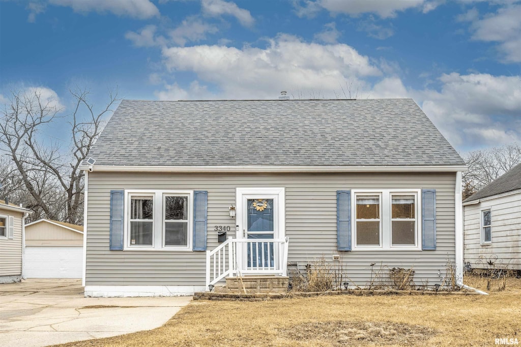 cape cod house with a shingled roof, an outdoor structure, and a detached garage