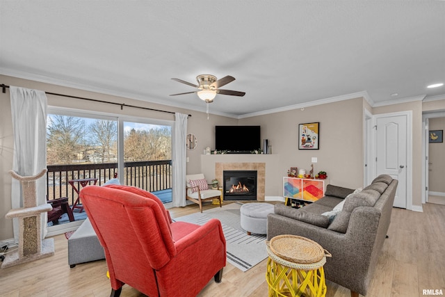 living room featuring a tiled fireplace, ceiling fan, ornamental molding, and light hardwood / wood-style flooring