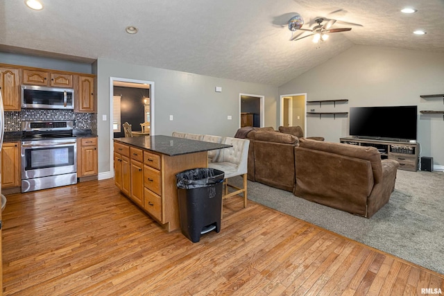 kitchen with vaulted ceiling, appliances with stainless steel finishes, light hardwood / wood-style flooring, and backsplash