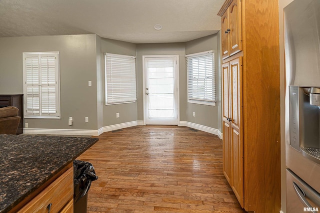 kitchen featuring stainless steel refrigerator with ice dispenser, a textured ceiling, light hardwood / wood-style floors, and dark stone counters