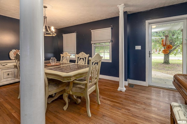 dining space featuring ornate columns, wood-type flooring, a textured ceiling, and a chandelier