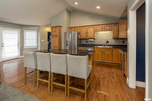 kitchen with lofted ceiling, a kitchen island, a kitchen bar, sink, and stainless steel appliances