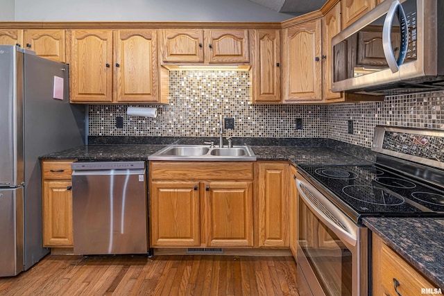 kitchen with appliances with stainless steel finishes, tasteful backsplash, dark stone countertops, light hardwood / wood-style flooring, and sink