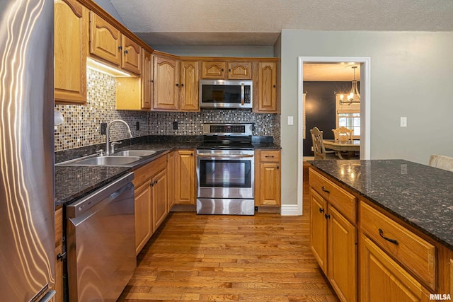 kitchen with light wood-type flooring, an inviting chandelier, stainless steel appliances, and a textured ceiling