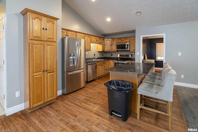 kitchen featuring a center island, a kitchen bar, stainless steel appliances, sink, and vaulted ceiling