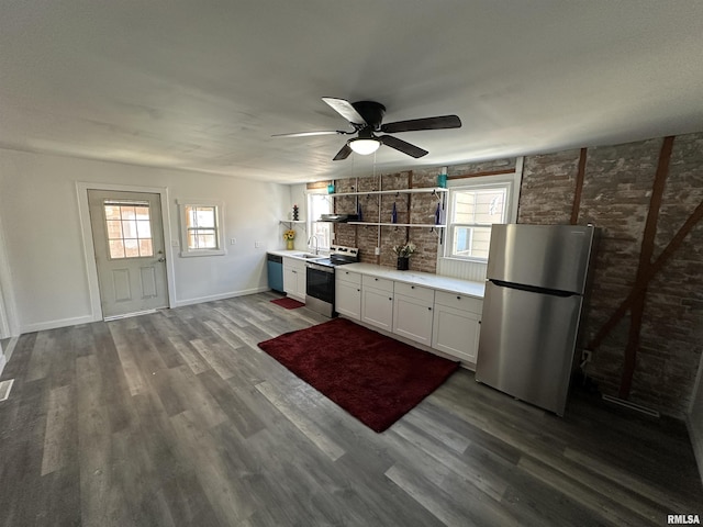 kitchen with brick wall, white cabinets, appliances with stainless steel finishes, dark hardwood / wood-style flooring, and sink