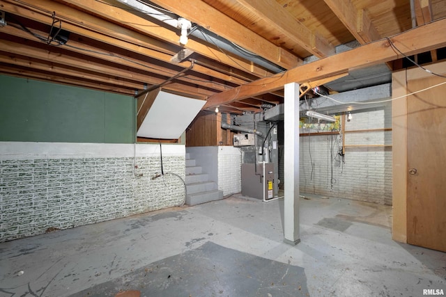 basement featuring brick wall and heating unit