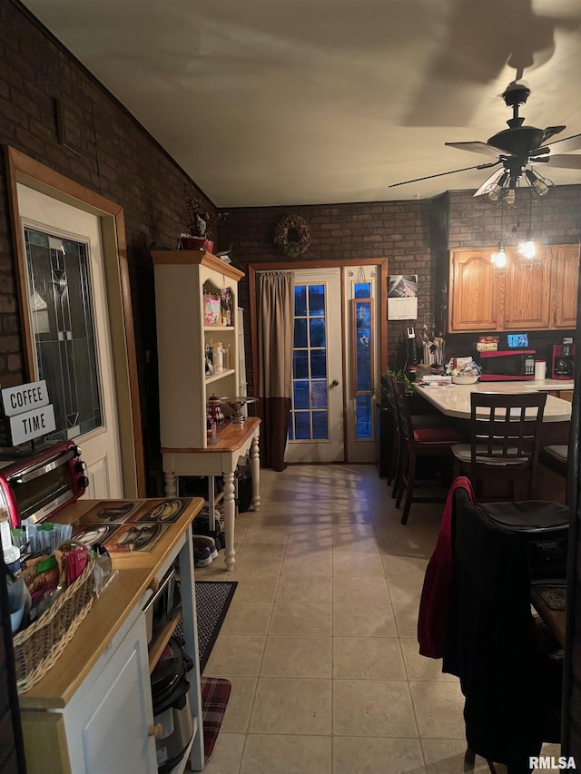 kitchen with light tile patterned floors, brick wall, and ceiling fan