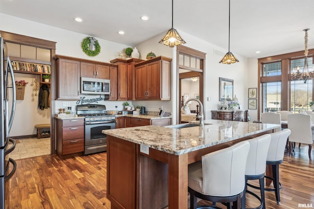 kitchen featuring light stone countertops, appliances with stainless steel finishes, decorative light fixtures, an inviting chandelier, and sink