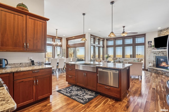 kitchen featuring light stone countertops, decorative light fixtures, a stone fireplace, sink, and stainless steel dishwasher