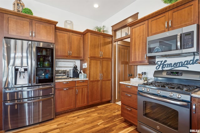 kitchen featuring appliances with stainless steel finishes, light hardwood / wood-style floors, and light stone counters