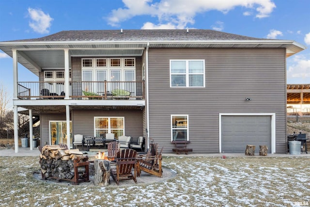 snow covered back of property with a garage and a fire pit