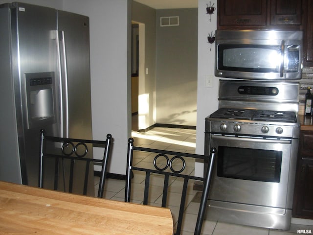 kitchen with stainless steel appliances, dark brown cabinets, tile patterned floors, and wood counters