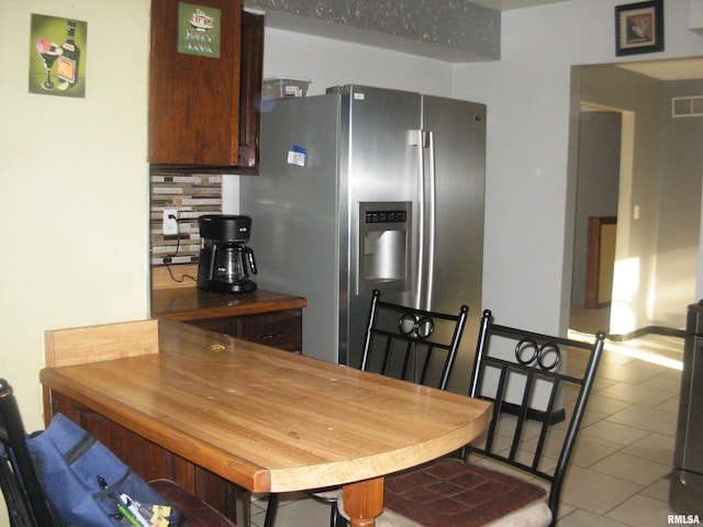 kitchen featuring tasteful backsplash, light tile patterned floors, and stainless steel fridge