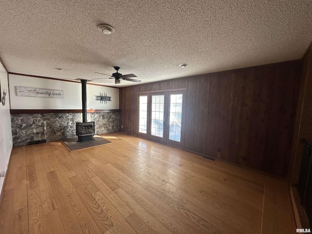 unfurnished living room featuring wood walls, ceiling fan, a wood stove, and light hardwood / wood-style flooring