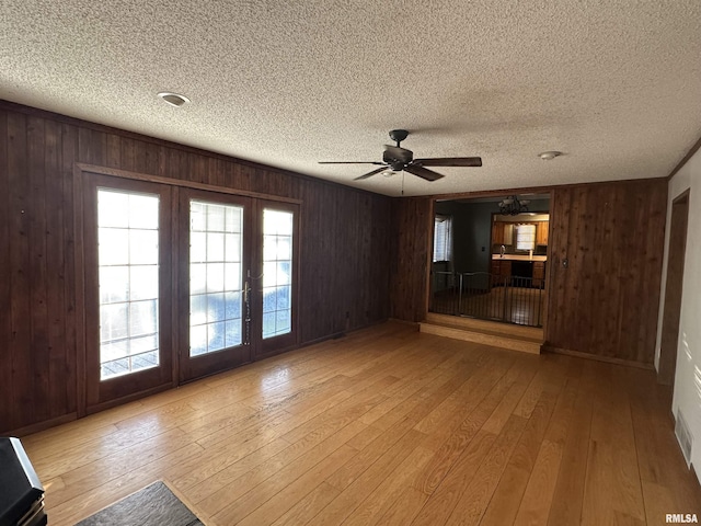 unfurnished living room with ceiling fan, light hardwood / wood-style floors, and wooden walls