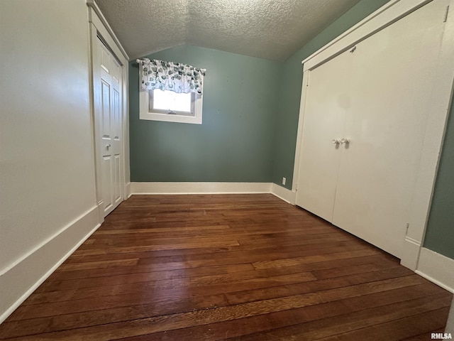 unfurnished bedroom featuring a textured ceiling, dark hardwood / wood-style floors, and lofted ceiling