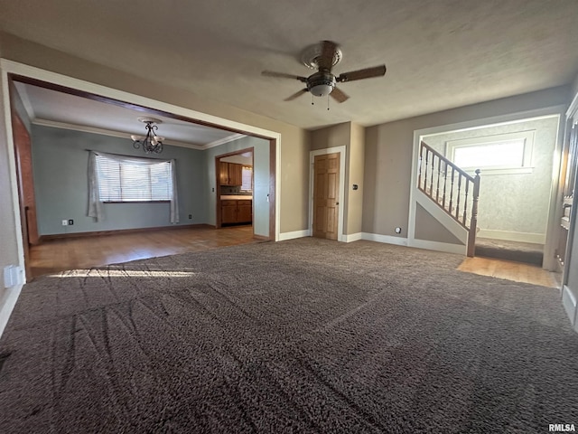 unfurnished living room featuring ceiling fan with notable chandelier, carpet, and ornamental molding