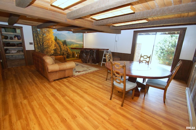 dining area featuring beamed ceiling, wood walls, and light hardwood / wood-style flooring