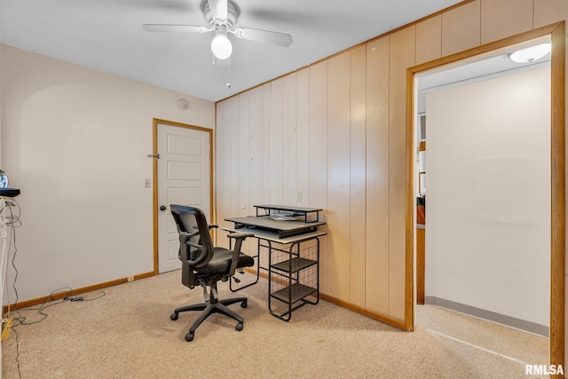 home office with ceiling fan, light colored carpet, and wood walls