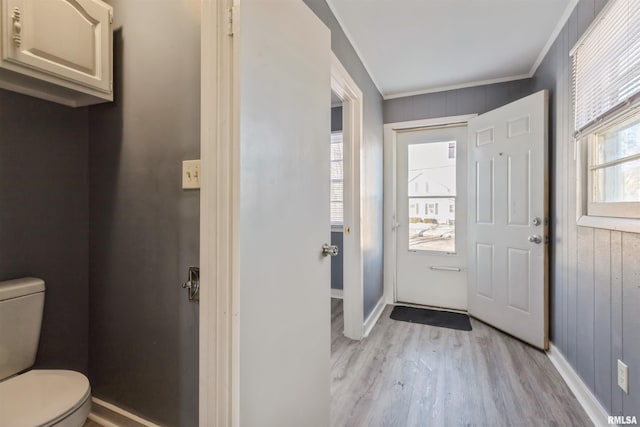 entrance foyer with wood walls, a healthy amount of sunlight, ornamental molding, and light hardwood / wood-style floors