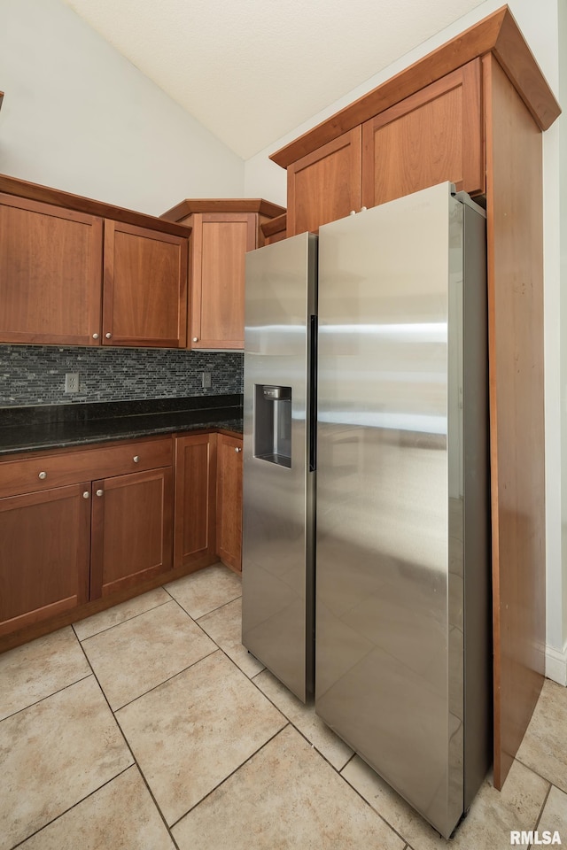 kitchen with tasteful backsplash, dark stone countertops, stainless steel fridge, and light tile patterned floors