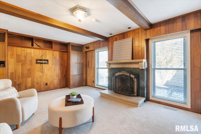 carpeted living area featuring beamed ceiling, visible vents, a fireplace with raised hearth, wooden walls, and baseboards