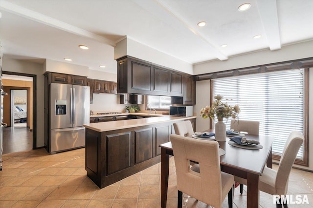 kitchen with a peninsula, light countertops, dark brown cabinetry, beamed ceiling, and stainless steel fridge