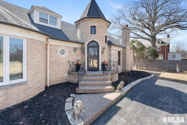 view of front facade featuring a chimney, fence, brick siding, and a shingled roof