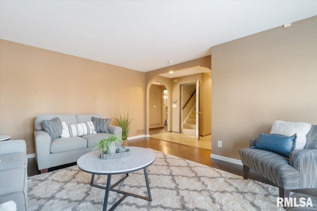 living room featuring arched walkways, stairway, baseboards, and wood finished floors