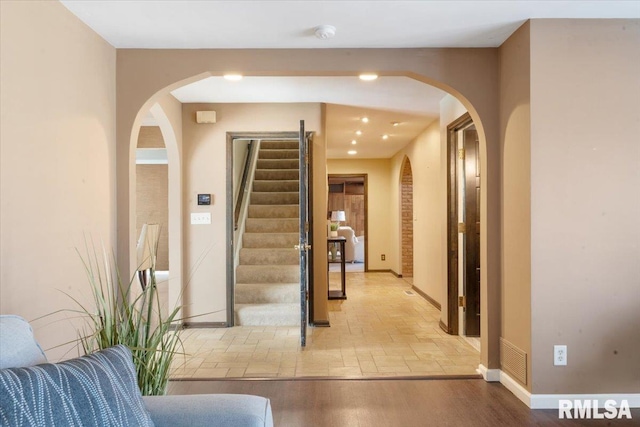 hall featuring wood finished floors, stairway, baseboards, and arched walkways