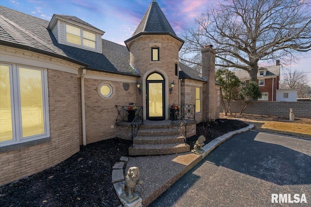 view of front of home featuring brick siding, a shingled roof, and fence