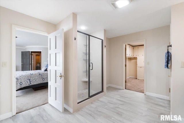 ensuite bathroom with ensuite bathroom, wood finished floors, a shower stall, baseboards, and a spacious closet