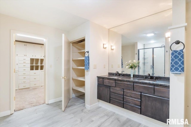 bathroom featuring double vanity, a shower stall, a walk in closet, and a sink