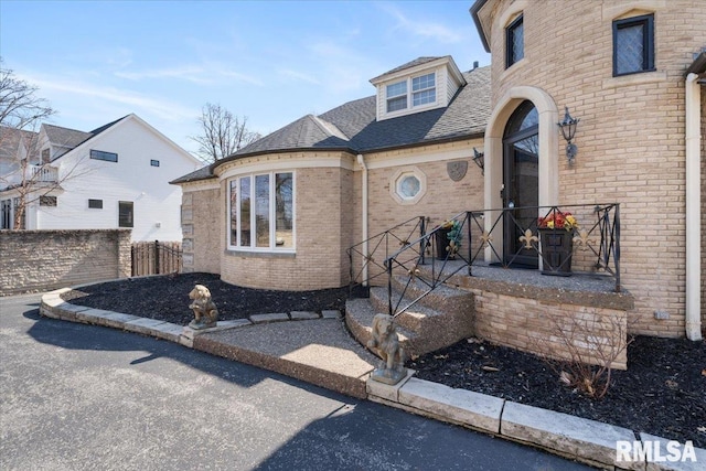 view of front of property with brick siding, roof with shingles, and fence