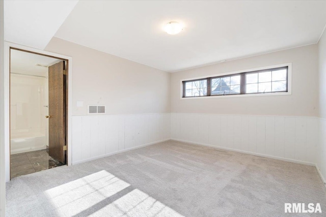 carpeted spare room with visible vents and a wainscoted wall