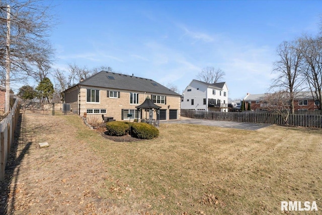 rear view of house featuring a garage, a fenced backyard, a lawn, and driveway