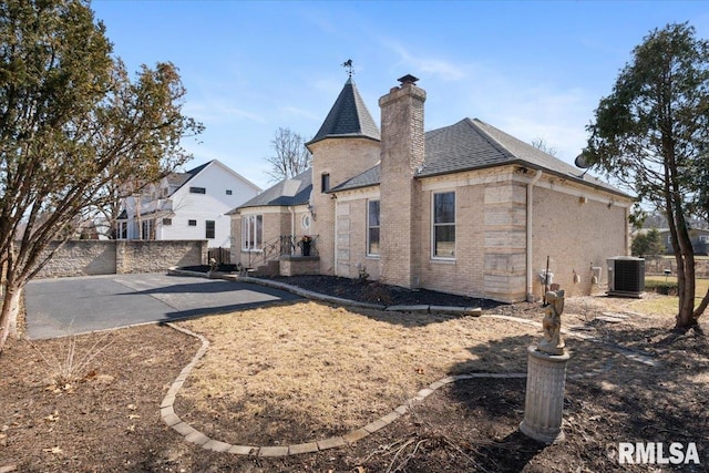 back of house with fence, roof with shingles, brick siding, central AC unit, and a chimney