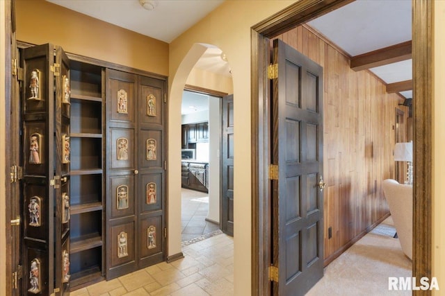 hallway with arched walkways, wood walls, and stone tile flooring