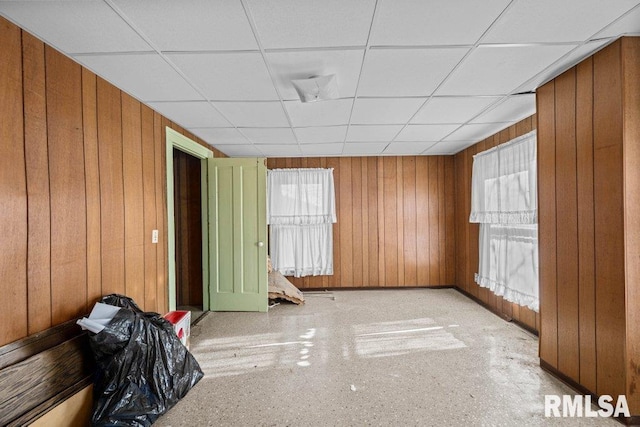 unfurnished room with a drop ceiling and wooden walls