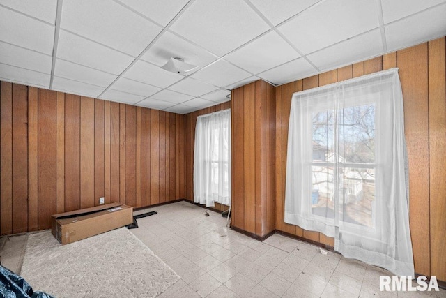 empty room with a paneled ceiling, a wealth of natural light, and wooden walls