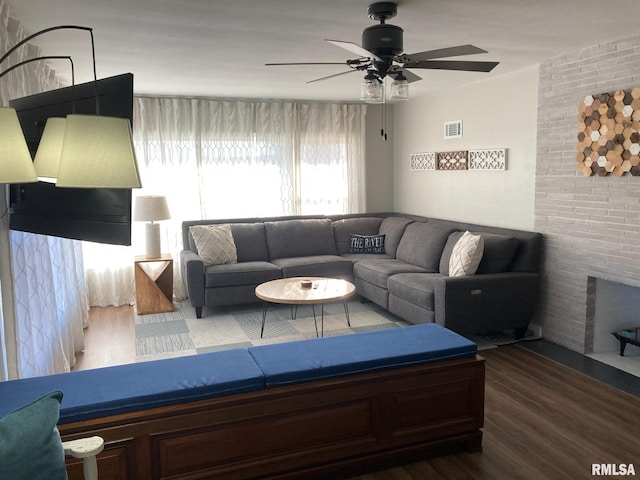 living room featuring a brick fireplace, brick wall, dark hardwood / wood-style floors, and ceiling fan