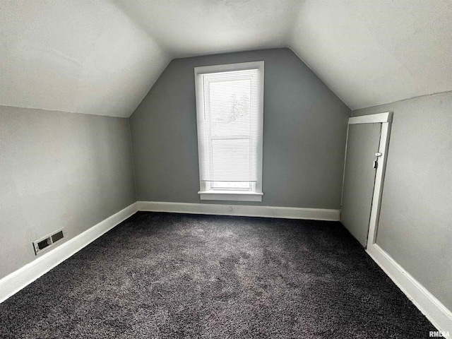 additional living space with vaulted ceiling, a wealth of natural light, and dark colored carpet