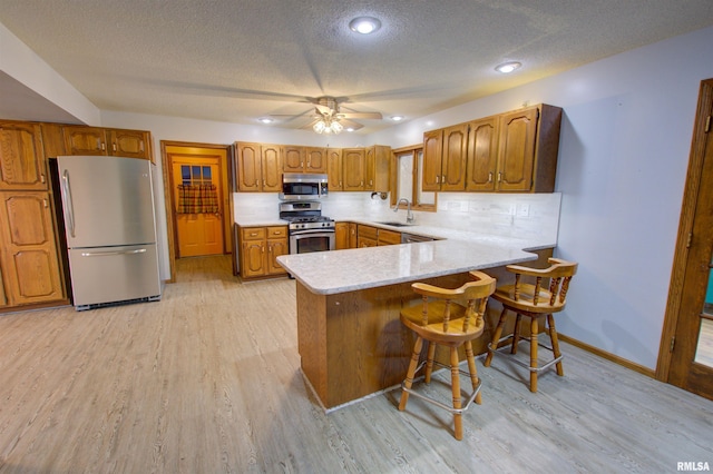 591 Breezy Point Dr, Clinton, IA 52732 - kitchen with appliances with stainless steel finishes, brown cabinets, a peninsula, light countertops, and light wood-style floors