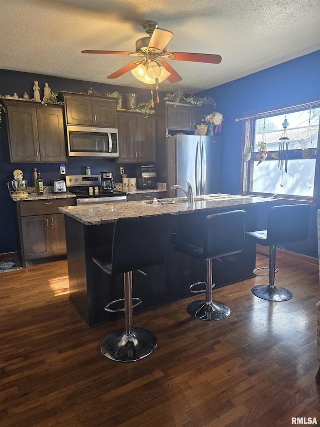 kitchen featuring sink, appliances with stainless steel finishes, a kitchen island with sink, a kitchen breakfast bar, and dark hardwood / wood-style flooring