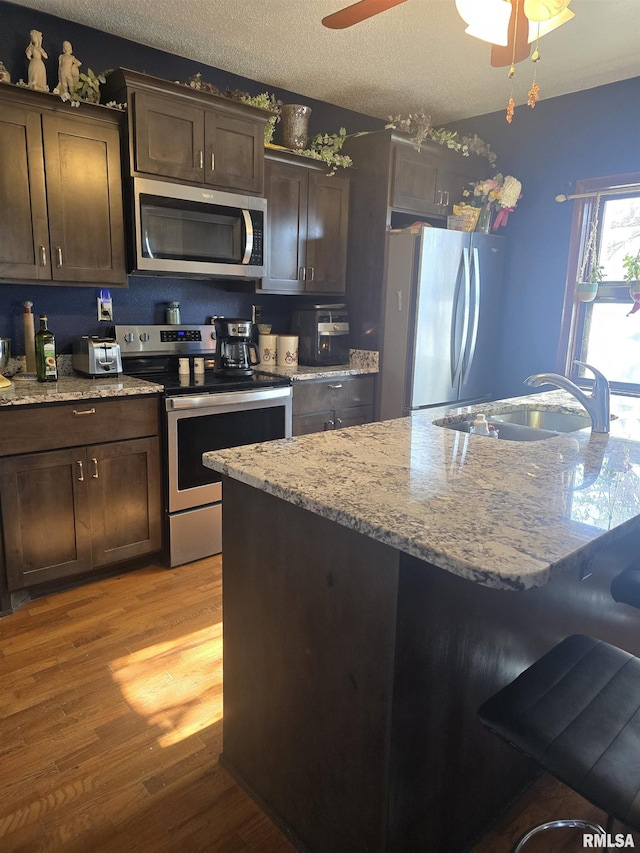 kitchen with sink, ceiling fan, stainless steel appliances, dark brown cabinets, and light wood-type flooring